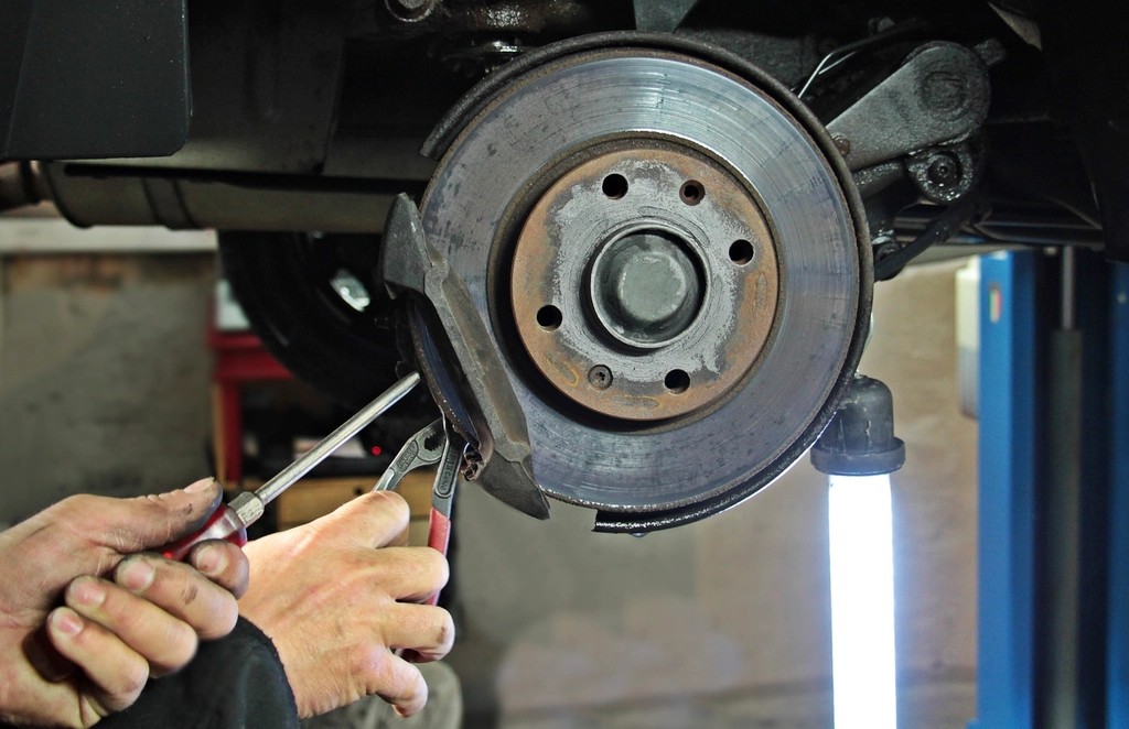 Handen van een monteur werken aan de remschijf en remklauw van een auto op de brug
