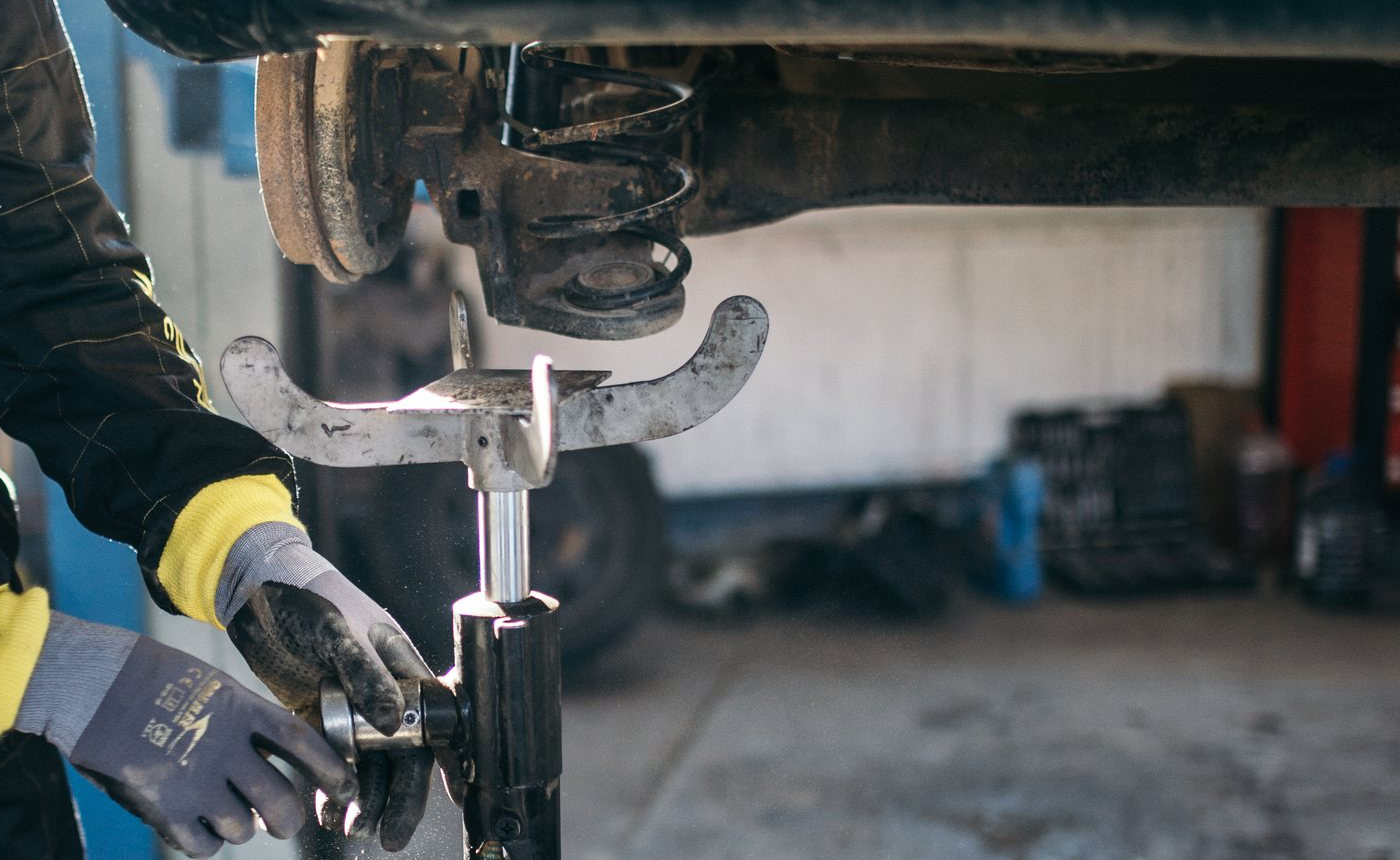 Monteur werkt met een krik onder een opgetilde auto in de werkplaats